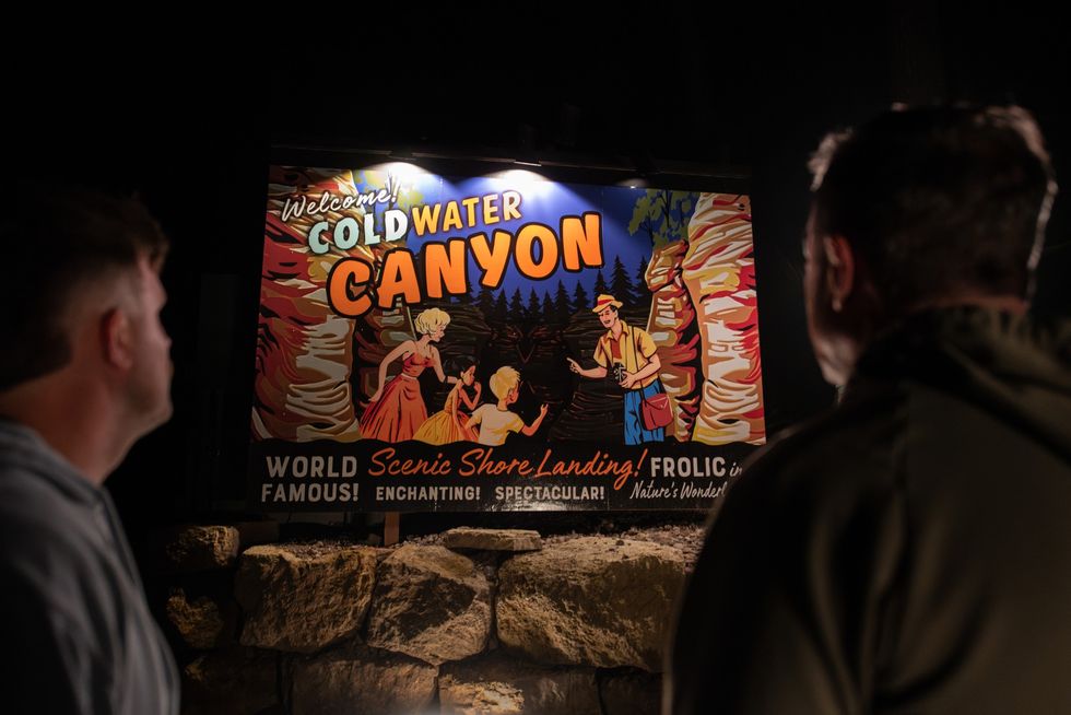 Two people observe a colorful "Cold Water Canyon" sign at night.