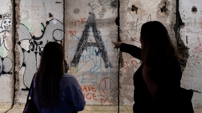 Two people observe graffiti on a crumbling concrete wall.