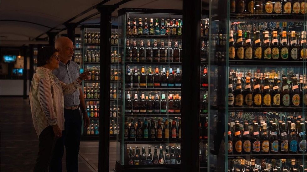 Two people observing a large display of assorted beer bottles.