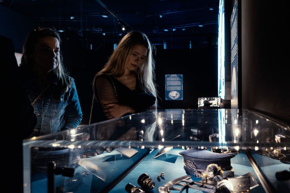 Two people observing Titanic artifacts in a dimly lit museum exhibit.