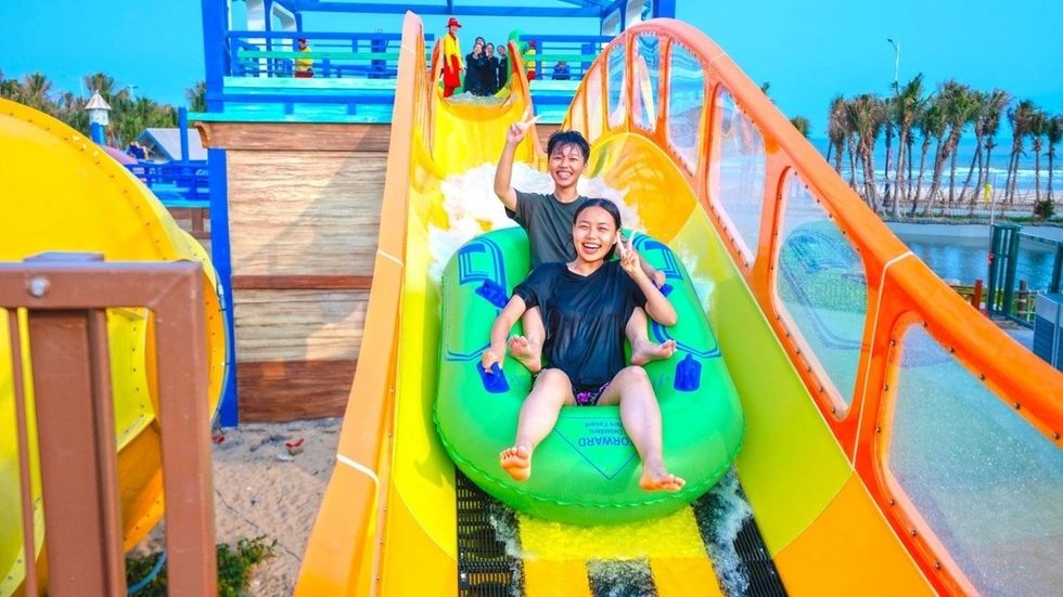 Two people on a green raft enjoy a colorful water slide.
