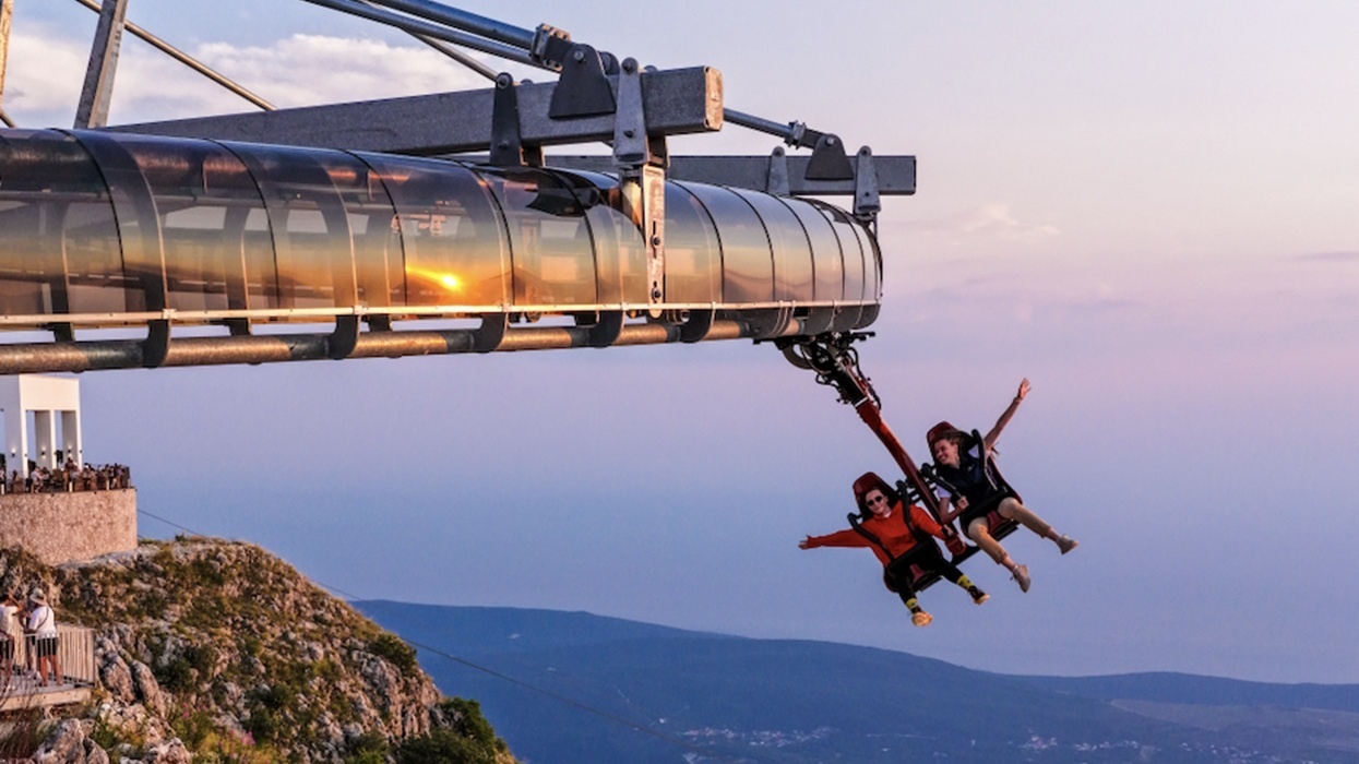 Two people on a Wie-Flyer at Lovćen National Park over a scenic landscape at sunset, joyfully spreading their arms.