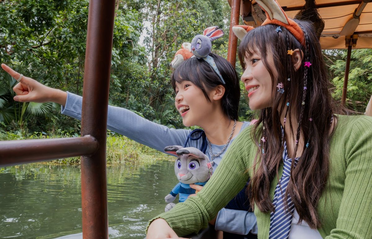Two people on Jungle Cruise ride at Hong Kong Disneyland joyfully pointing, surrounded by lush greenery.