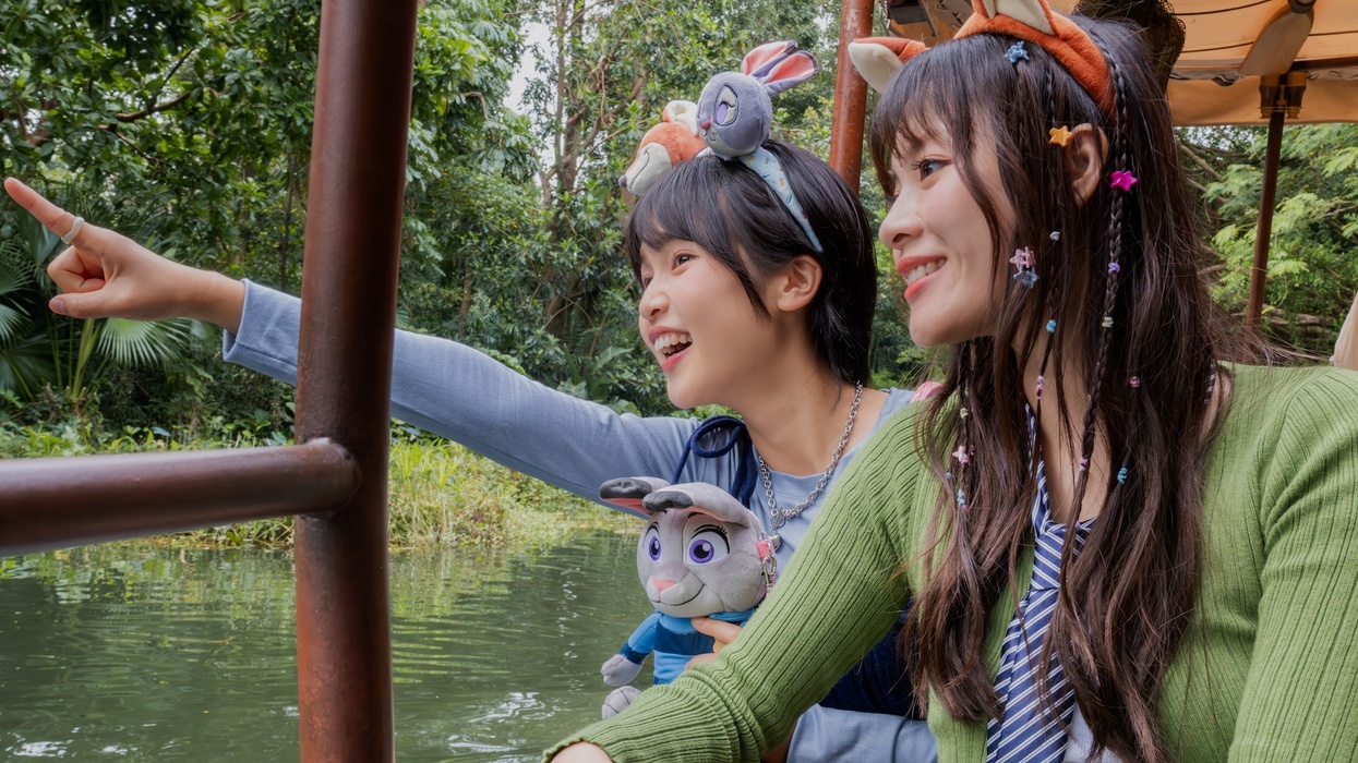 Two people on Jungle Cruise ride at Hong Kong Disneyland joyfully pointing, surrounded by lush greenery.
