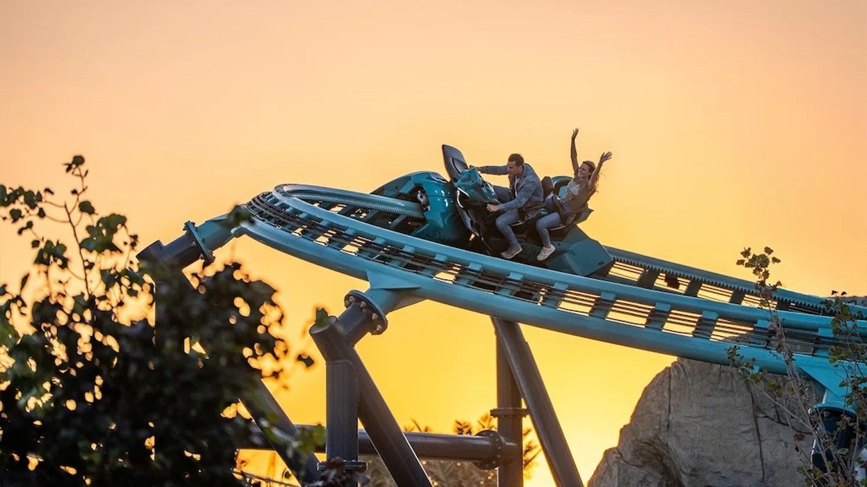 Two people on Maurer's Sea Stallion roller coaster at sunset, one with arms raised, at Six Flags Qiddiya