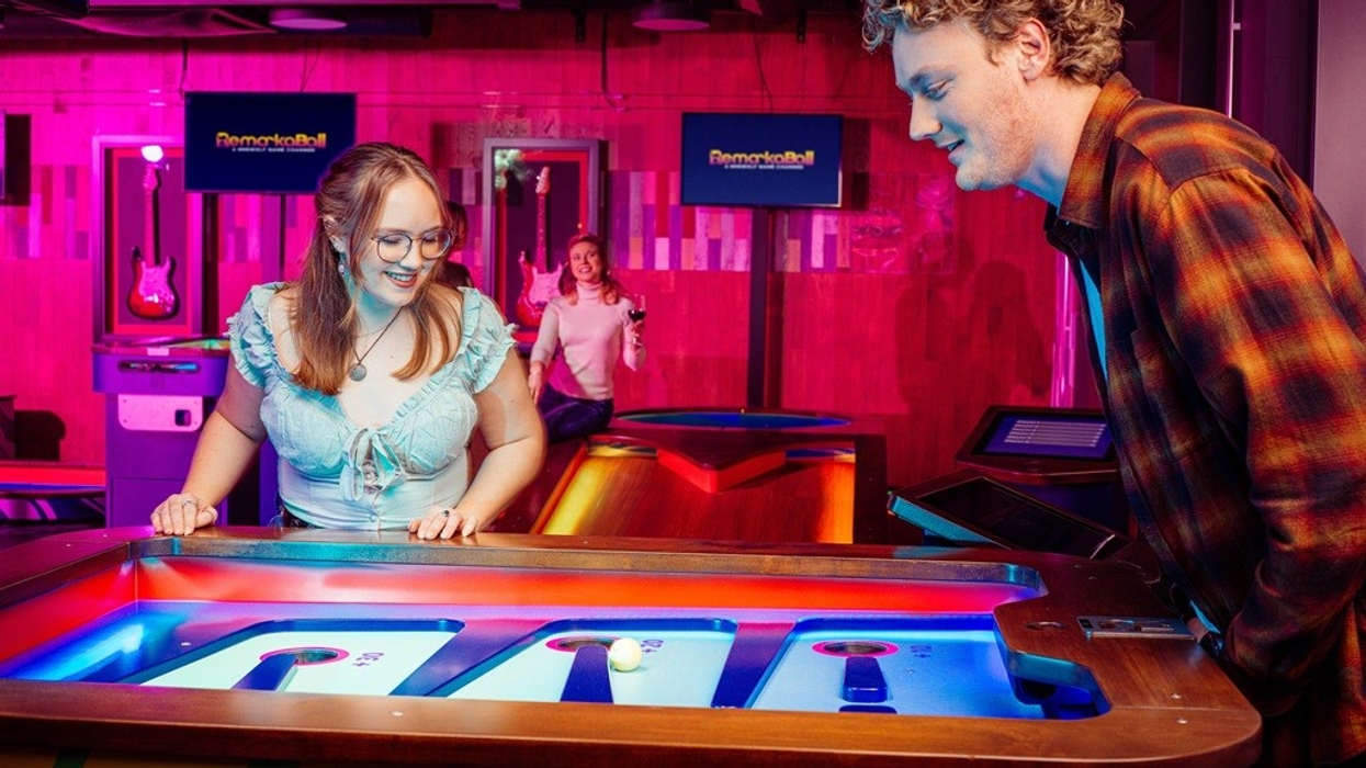 Two people play an arcade game under colorful neon lights.