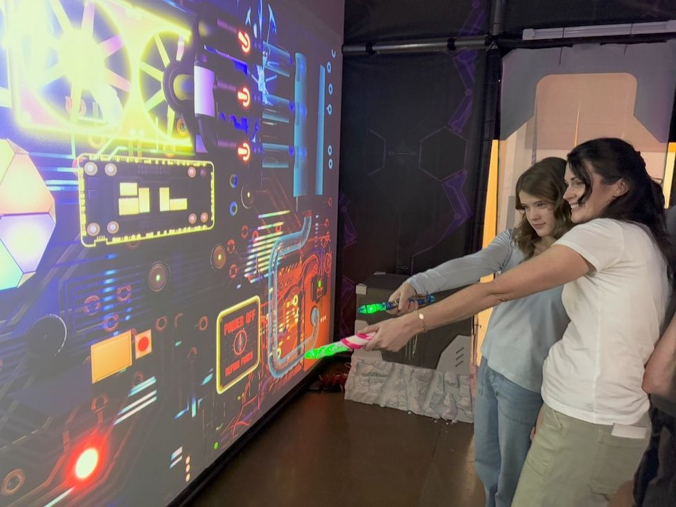 Two people play an interactive game, aiming at a colorful digital screen.