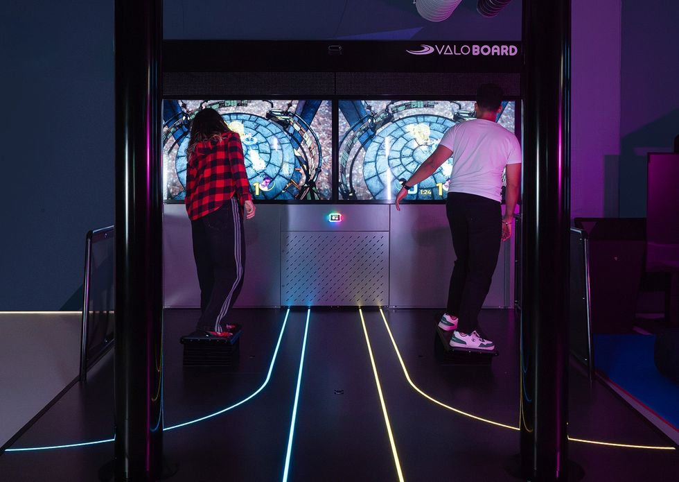 Two people playing a virtual reality game on ValoBoard with glowing floor lines.