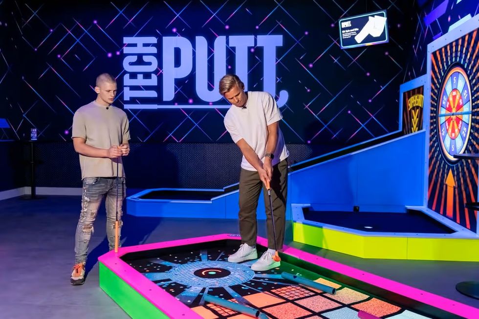 Two people playing mini golf from 360Golf indoors at a tech-themed course.