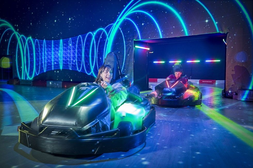 Two people race go-karts under colorful neon lights in a futuristic indoor track.