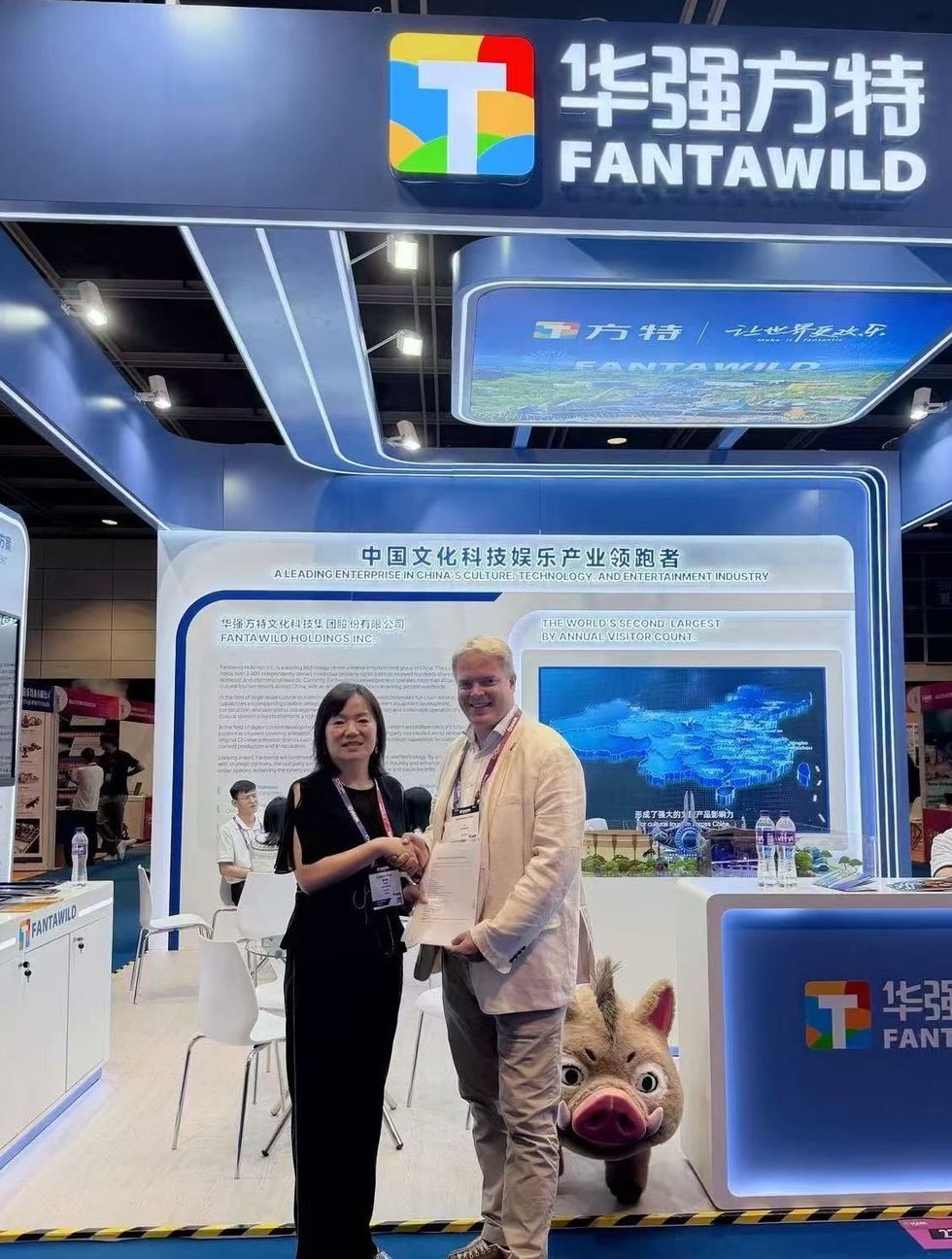 Two people shaking hands at Fantawild booth, with a character mascot in the background.