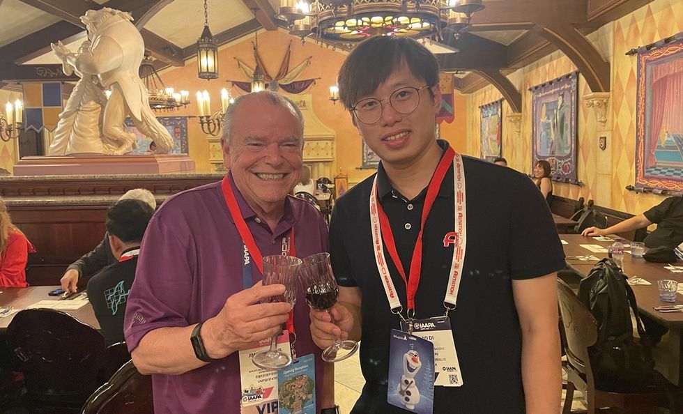 Two people smiling and holding wine glasses in a warmly lit, decorated room.