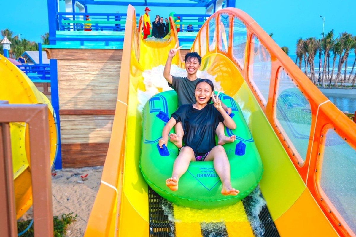 Two people smiling on a bright water slide in an amusement park.