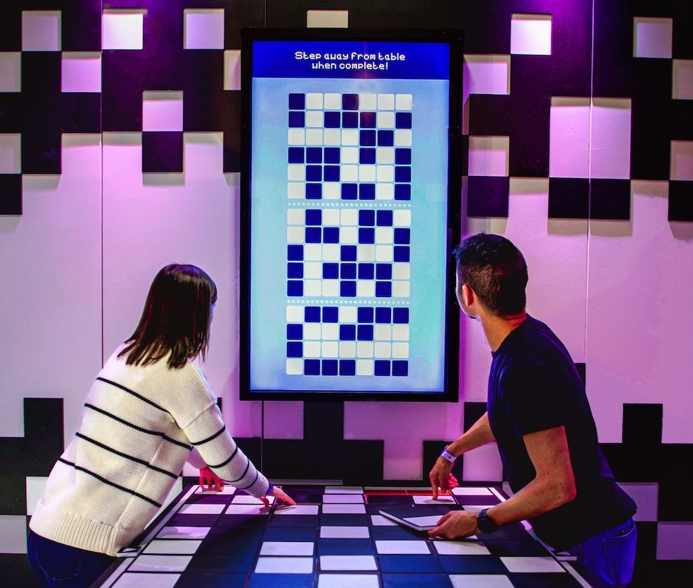 Two people solving a digital puzzle on a screen with a checkered floor pattern.