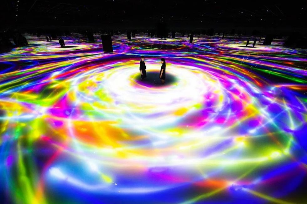 Two people stand amid vibrant swirling rainbow patterns on a reflective surface.