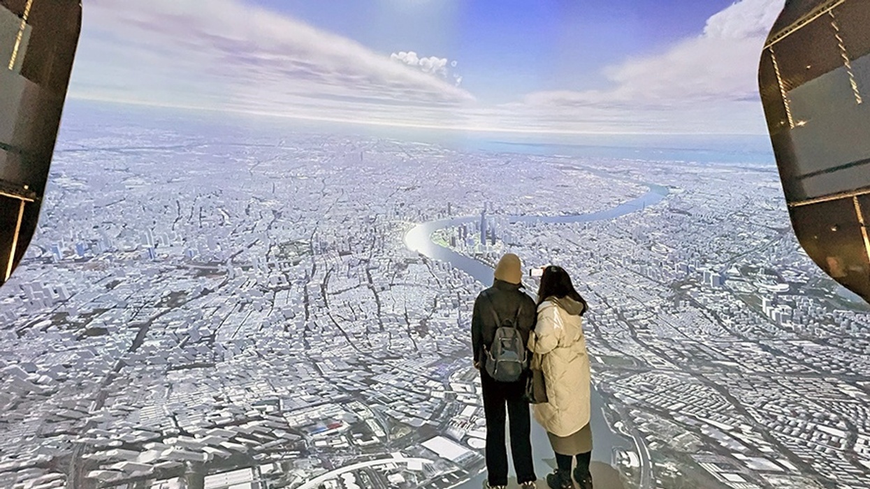 Two people stand on a platform overlooking a vast aerial city view.