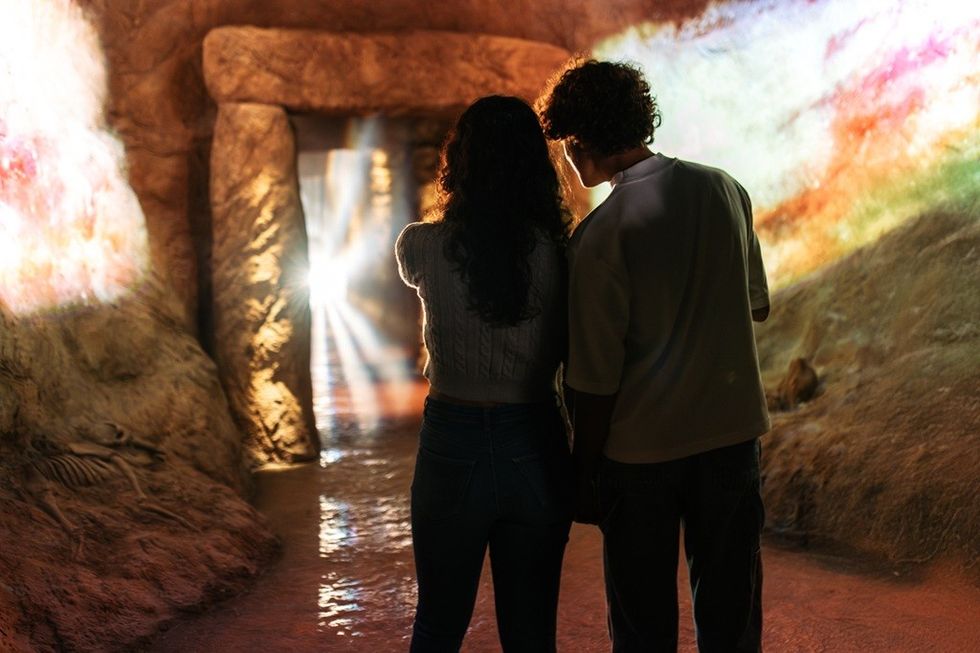 Two people standing inside a cave with colorful light reflections on the walls.