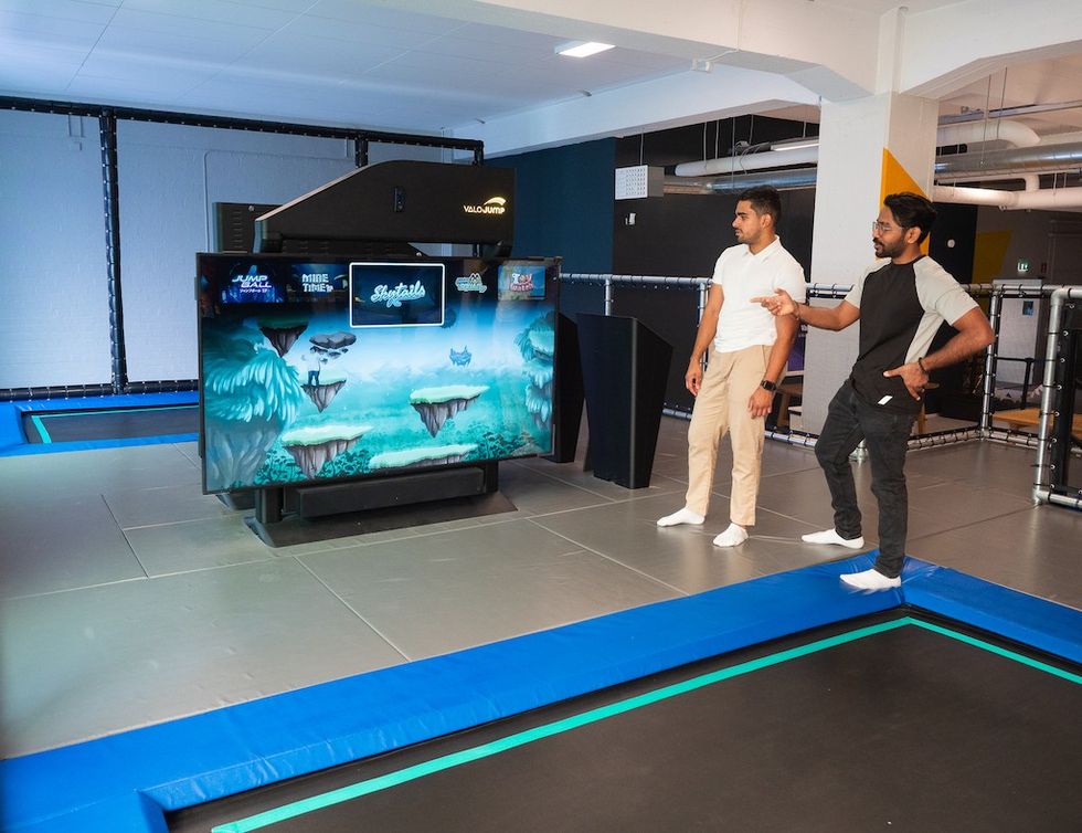 Two people standing near a large screen displaying a ValoJump game in an indoor facility.