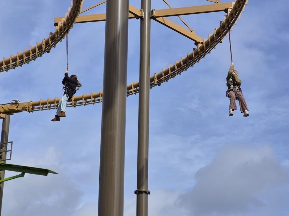 Two people suspended on ropes beneath a large, curving structure against a blue sky.