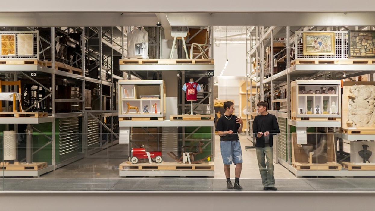 Two people talking in a modern museum (V&A East Storehouse) with items displayed on shelves.