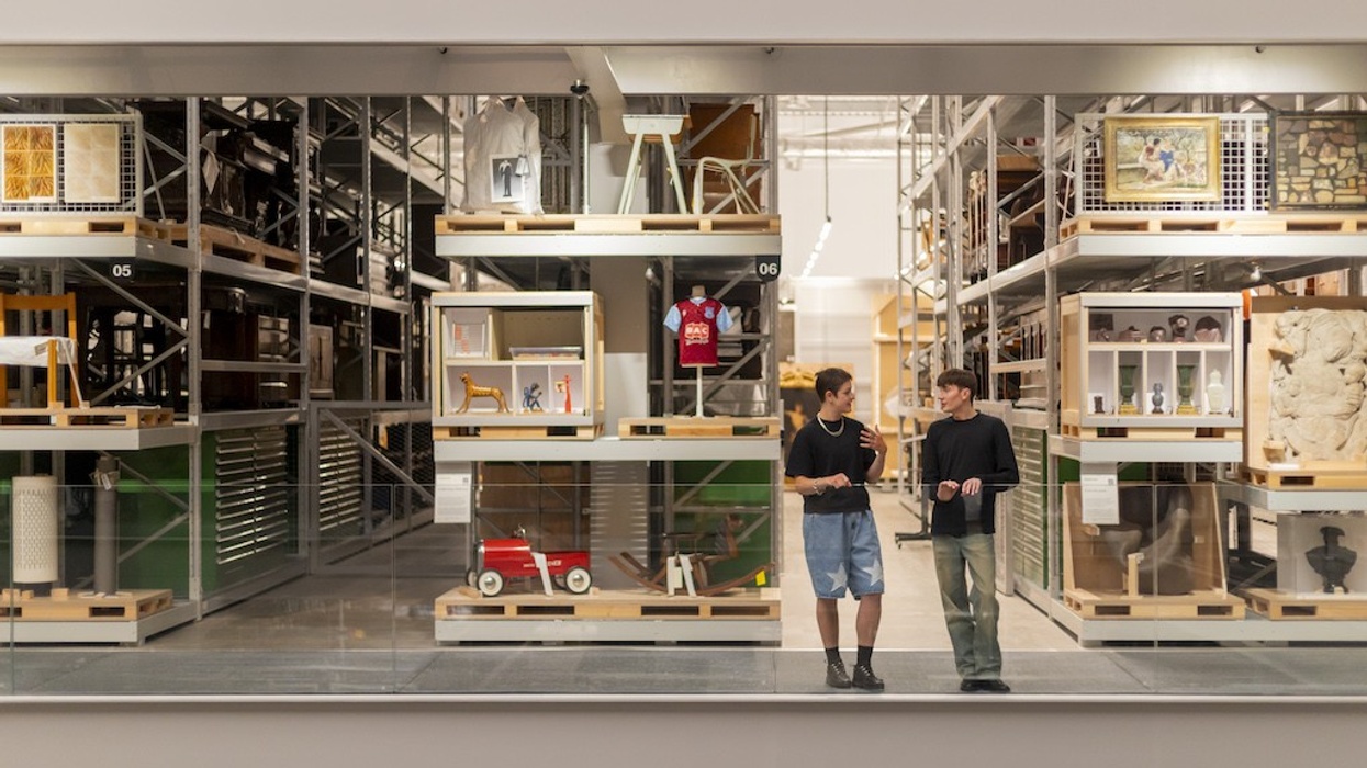 Two people talking in a modern museum (V&A East Storehouse) with items displayed on shelves.