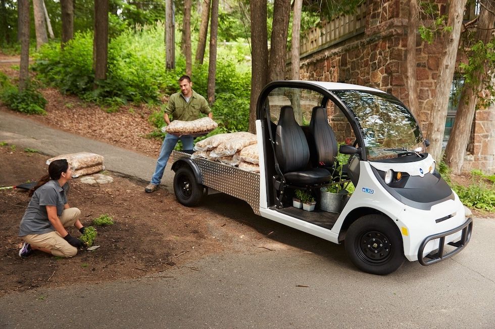 Two people unload mulch from a small utility vehicle in a wooded area.