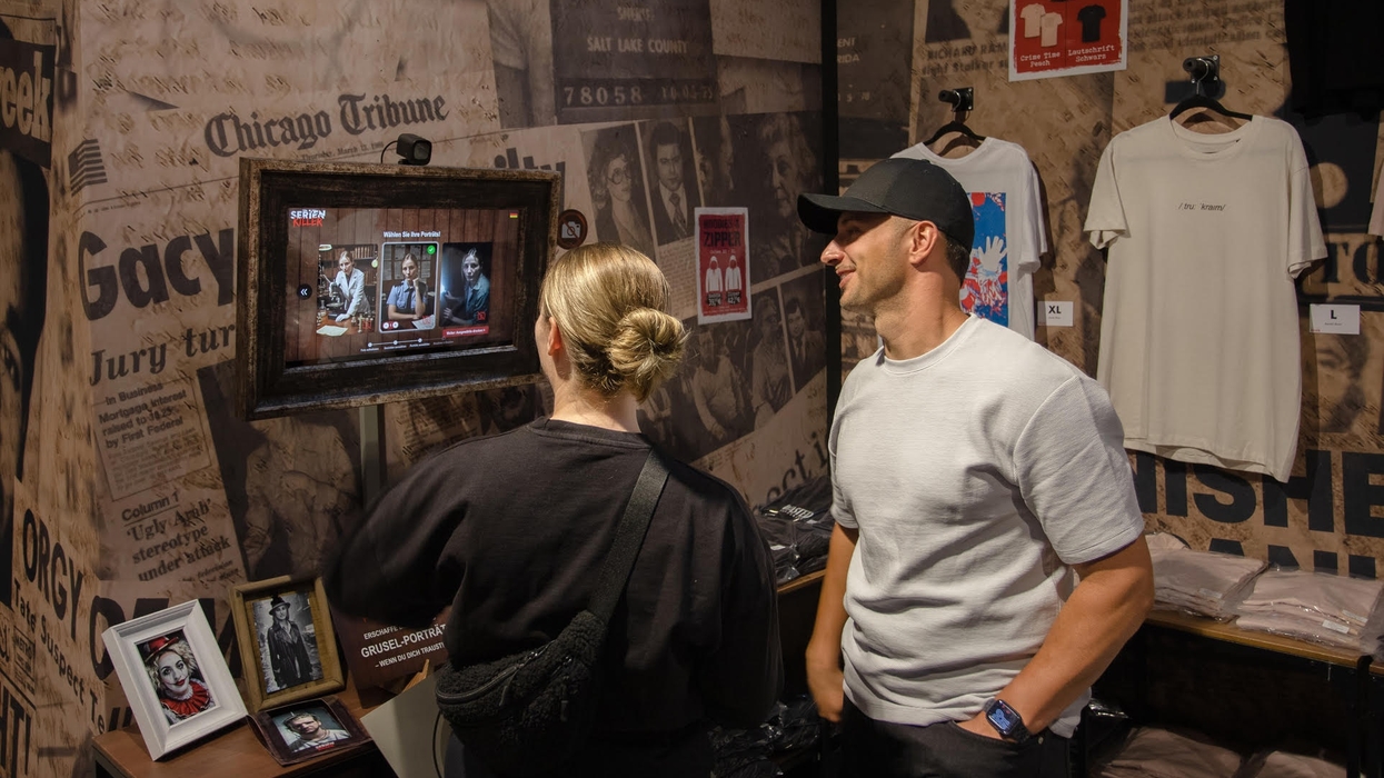 Two people view a crime-themed exhibit with newspaper clippings and framed photos.
