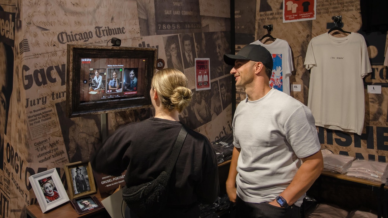 Two people view a crime-themed exhibit with newspaper clippings and framed photos.