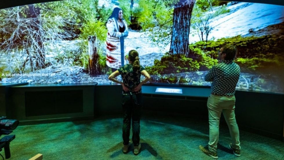 Two people view a large immersive screen displaying a nature scene.