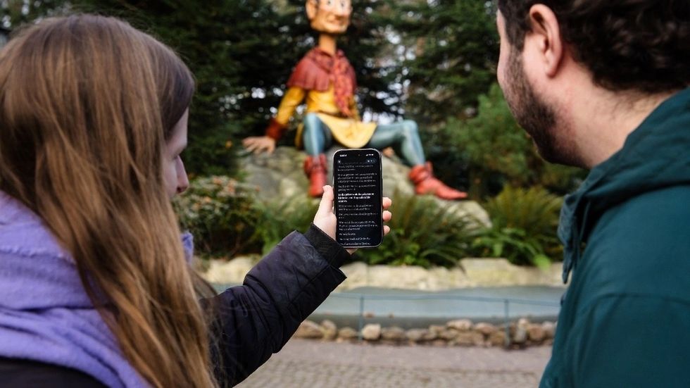 Two people view text on a phone in front of a giant puppet statue outdoors at Efteling