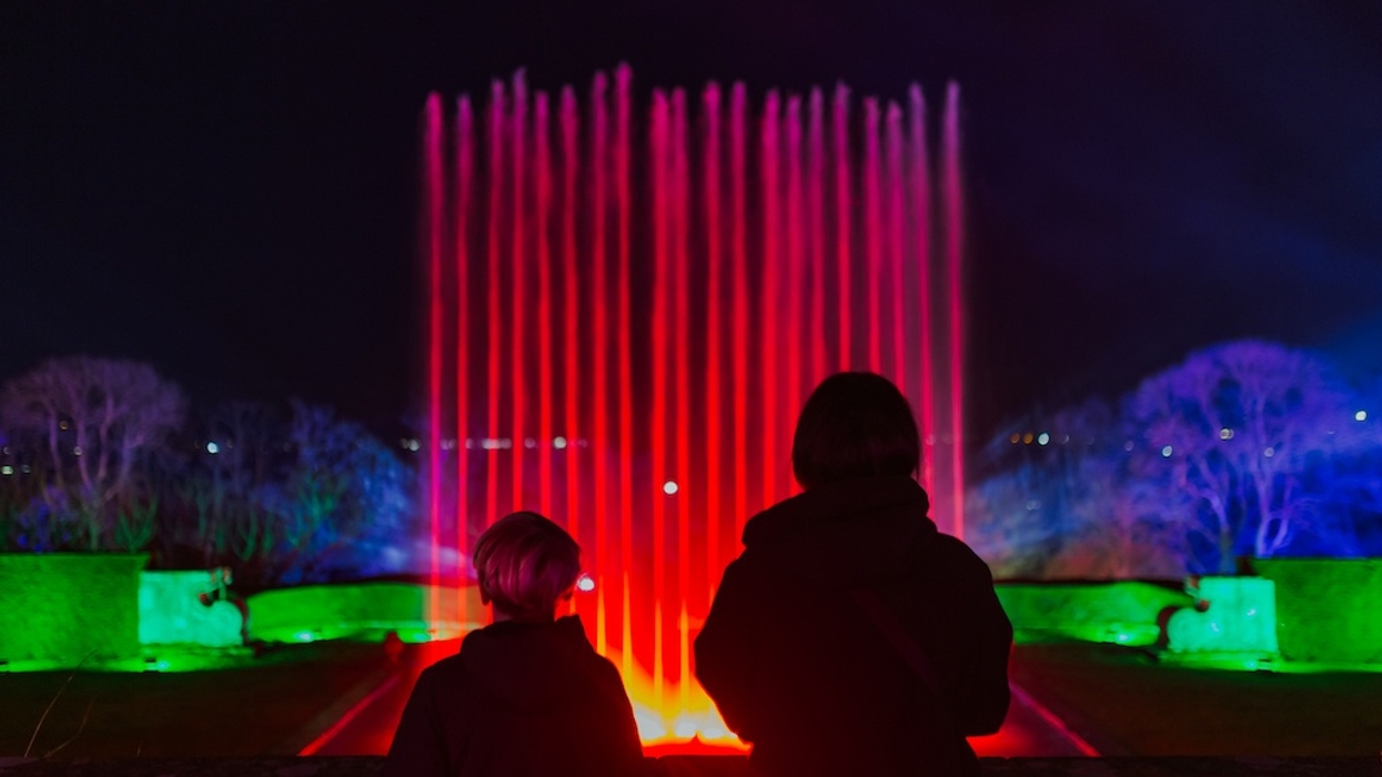 Two people watch a colorful illuminated fountain at night during Port Lympne Illuminated