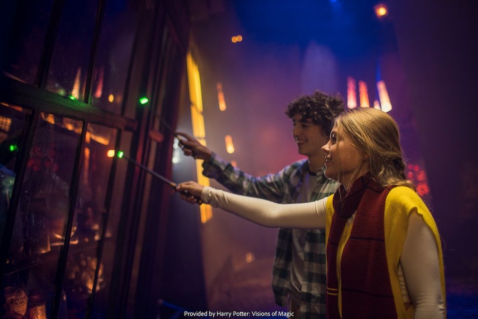 Two people waving wands in a dimly lit, magical setting at Harry Potter: Visions of Magic