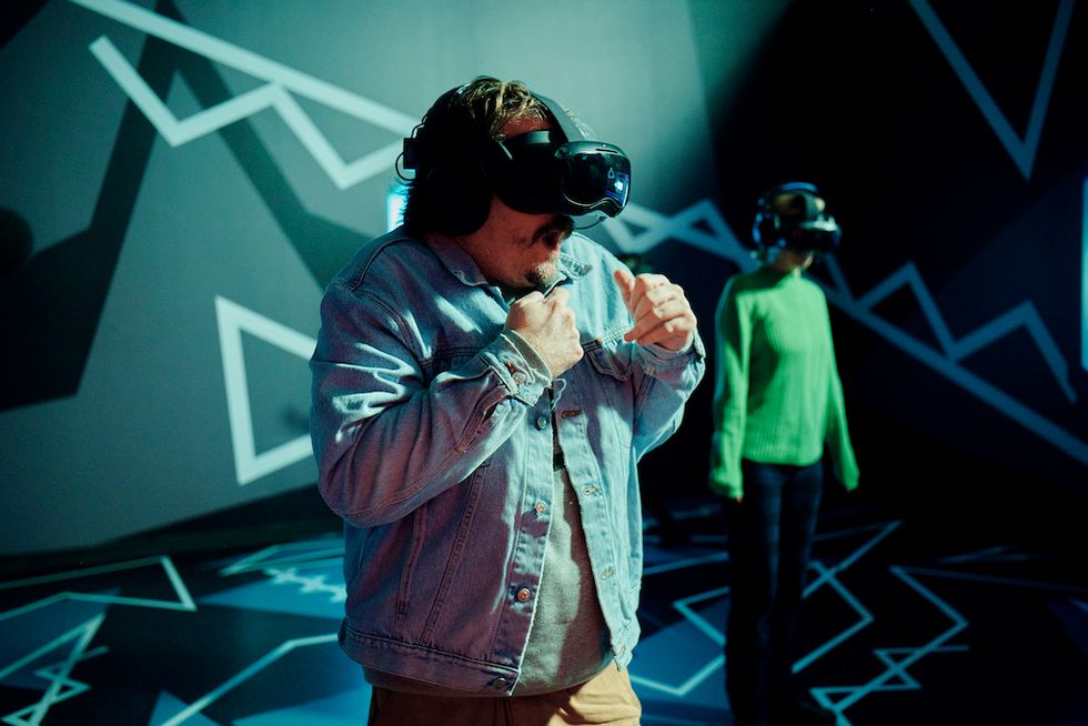 Two people wearing VR headsets in a geometric, neon-lit room.