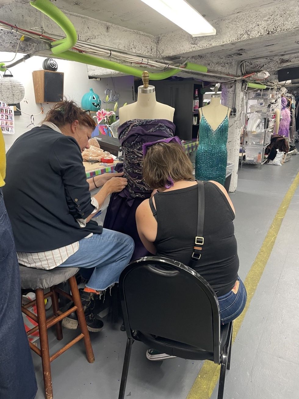 Two people working on a purple dress backstage on broadway's Death Becomes Her with mannequins.