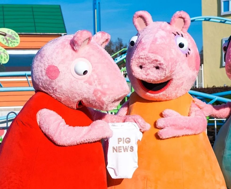 Two Peppa Pig characters hold a onesie that says "Pig News" at an amusement park.