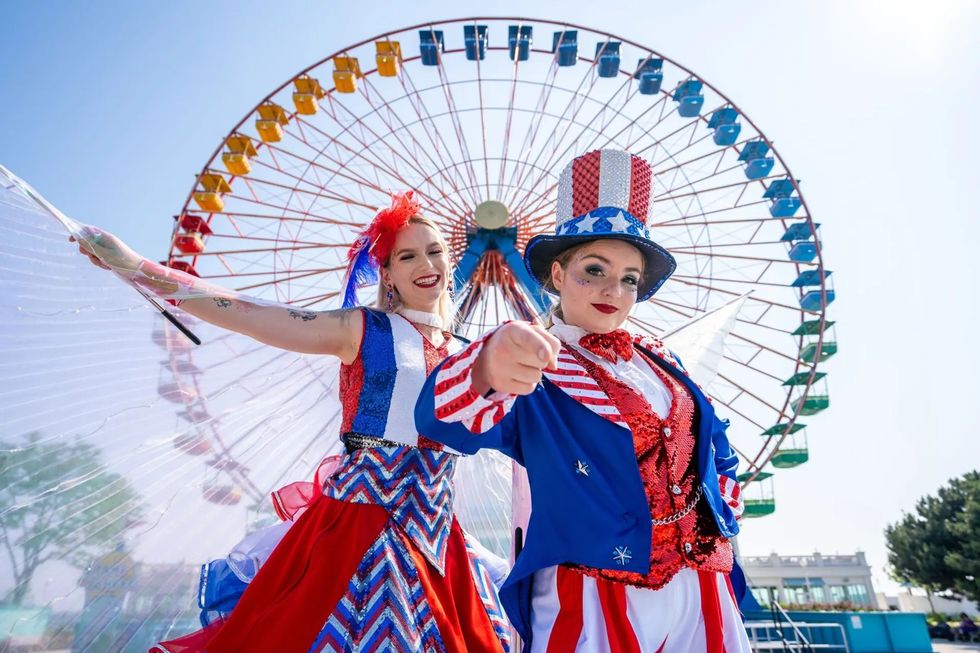 Two performers at Cedar Point in patriotic outfits near a Ferris wheel on a sunny day.