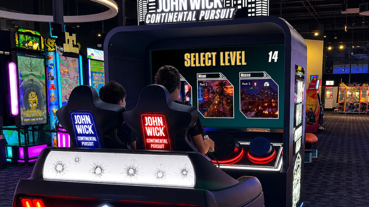 Two players use a John Wick arcade simulator, selecting a level in an illuminated arcade cabinet.