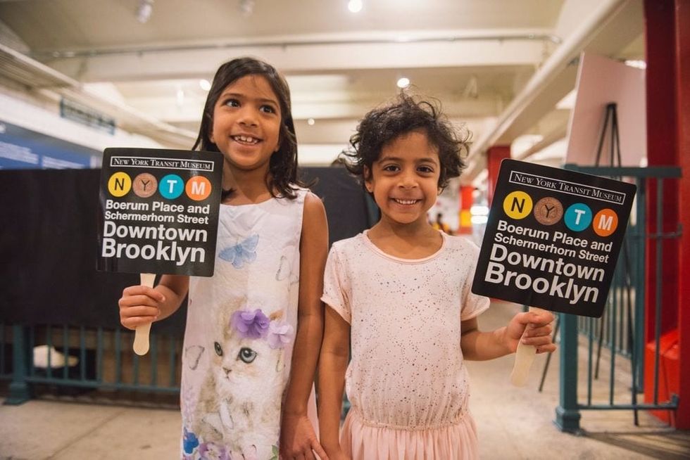 Two smiling children each holding a signage to Downtown Brooklyn