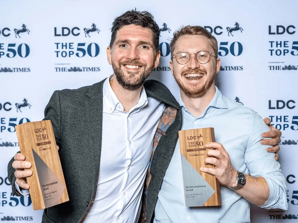 Two smiling men holding awards at LDC Top 50 event backdrop.