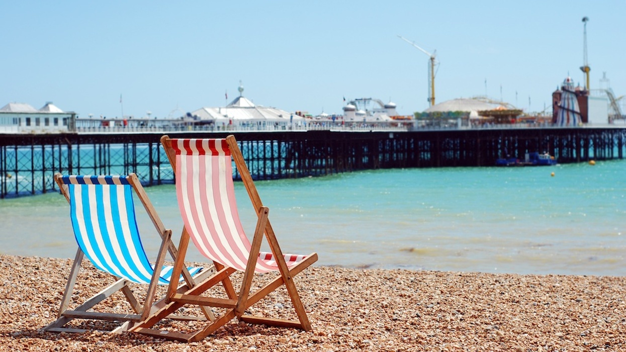 Two striped deck chairs on a pebble beach with a pier in the background.