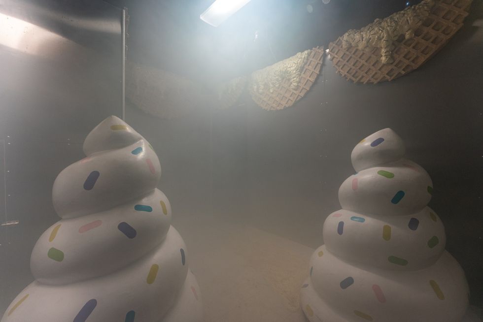 Two swirled sculptures with sprinkles in a foggy room, waffle patterns on wall.