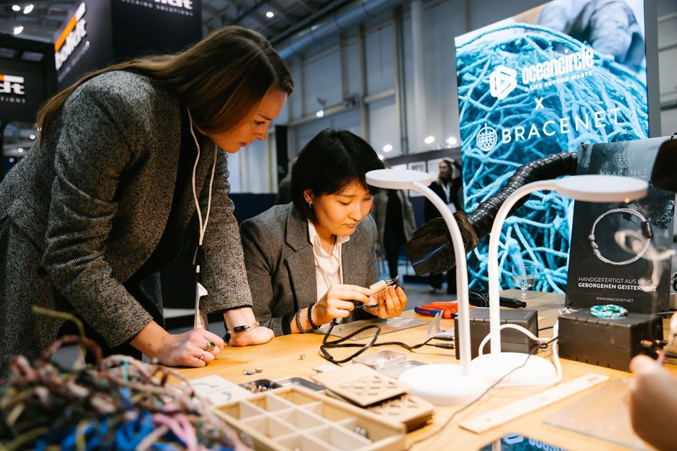 Two women crafting jewelry at an exhibition booth.