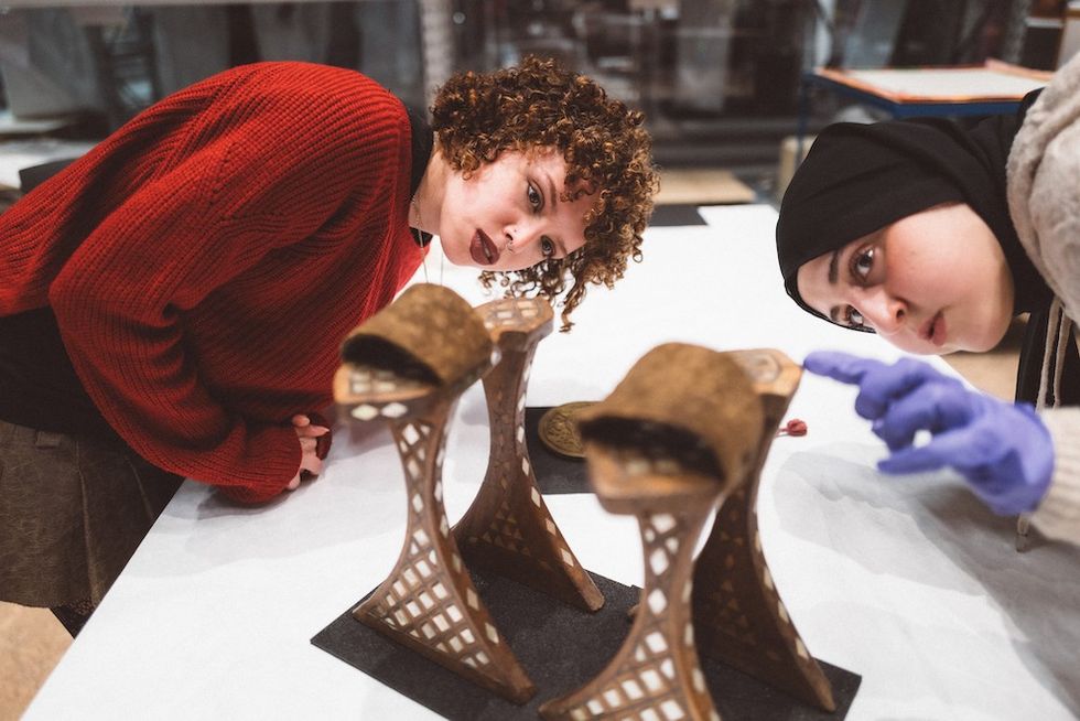 Two women examining intricately designed metal structures on a table.