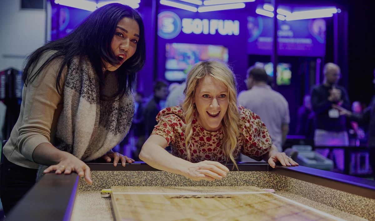 Two women excitedly playing shuffleboard at an indoor arcade.