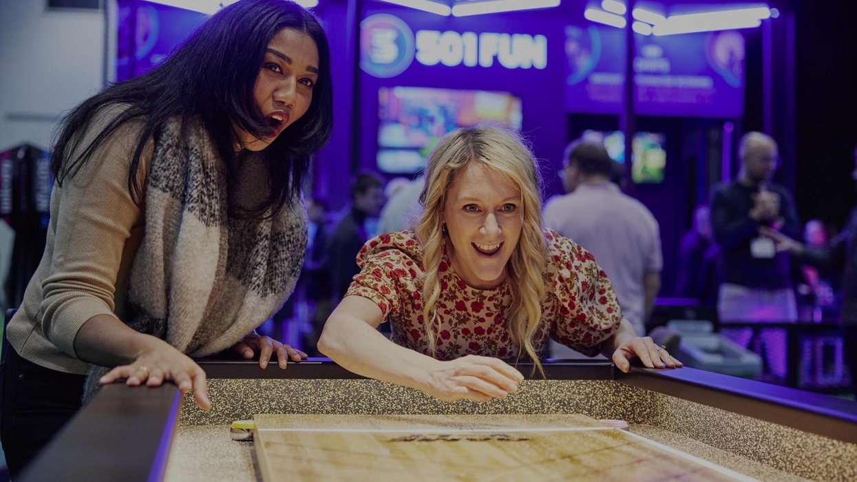 Two women excitedly playing shuffleboard at an indoor arcade.