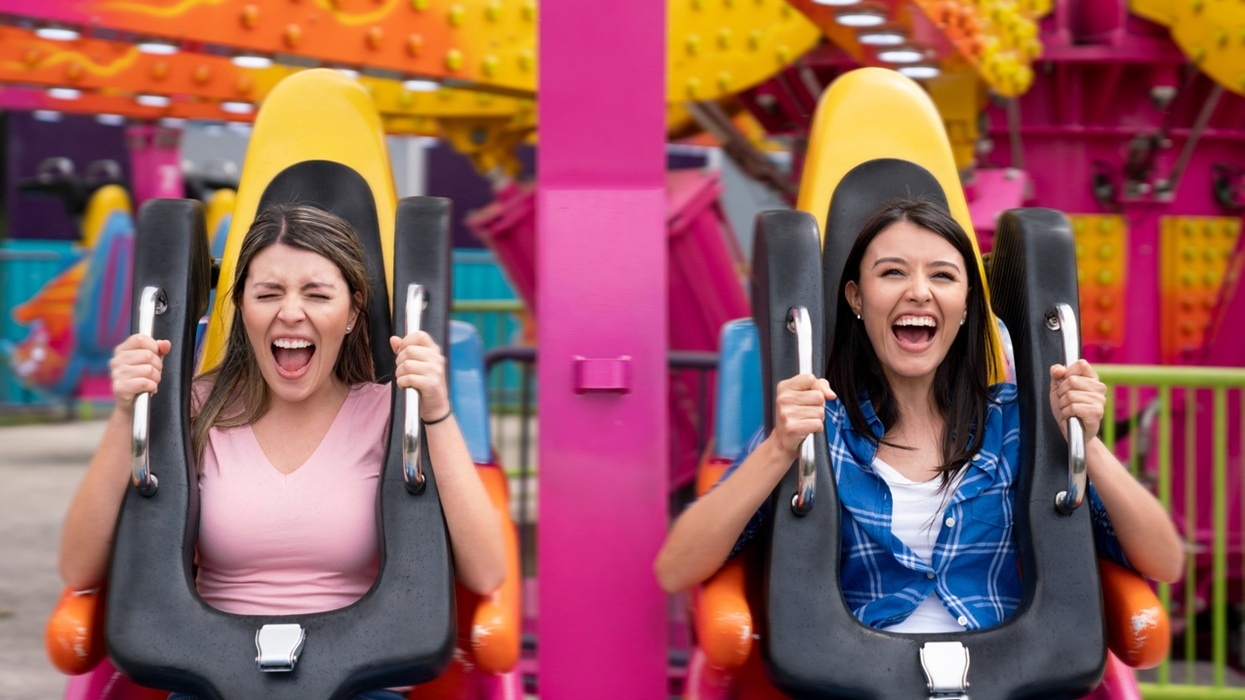 Two women excitedly riding a colourful amusement park ride.