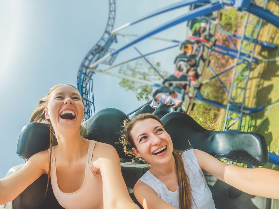 Two women laughing on a roller coaster ride under a clear blue sky.