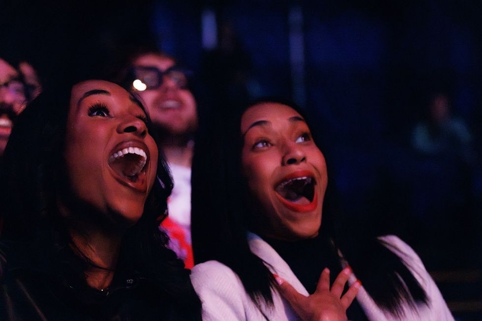 Two women, mouths wide open, express excitement in a dark setting at a Cirque du Soleil performance.