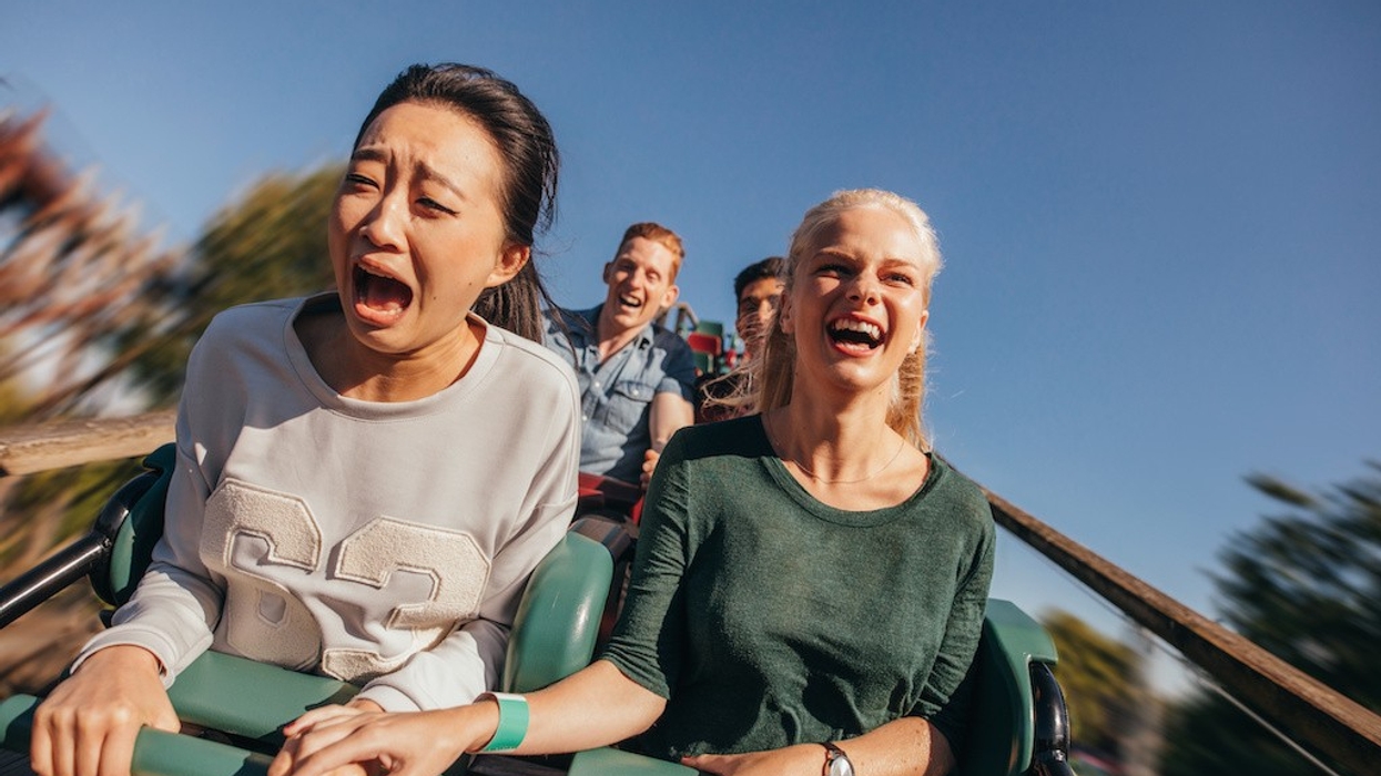 Two women on a roller coaster, one screaming, one laughing, holding hands.