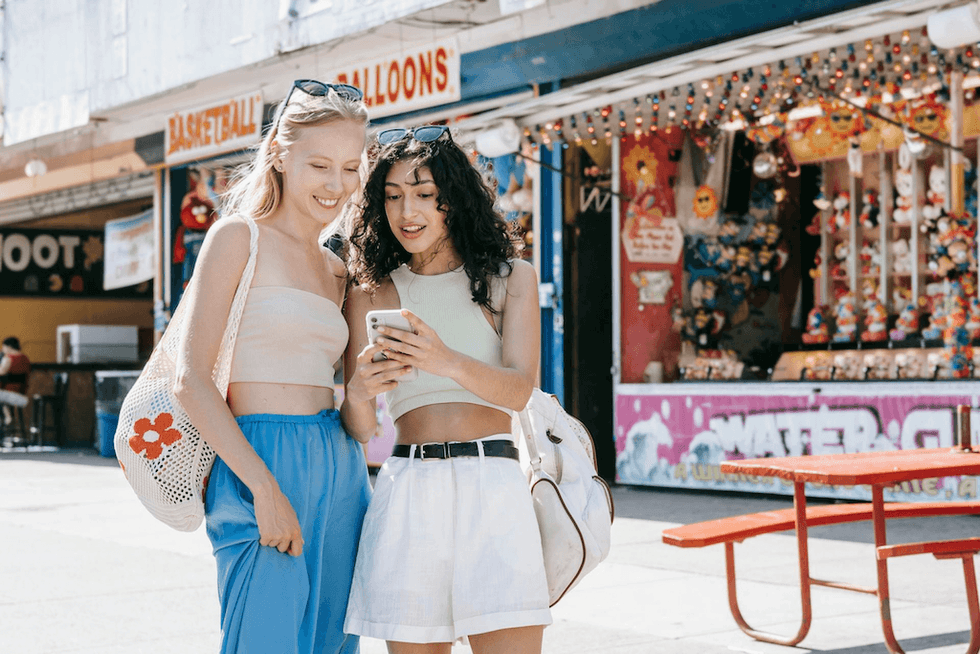 Two women smiling and looking at a phone in an amusement park.